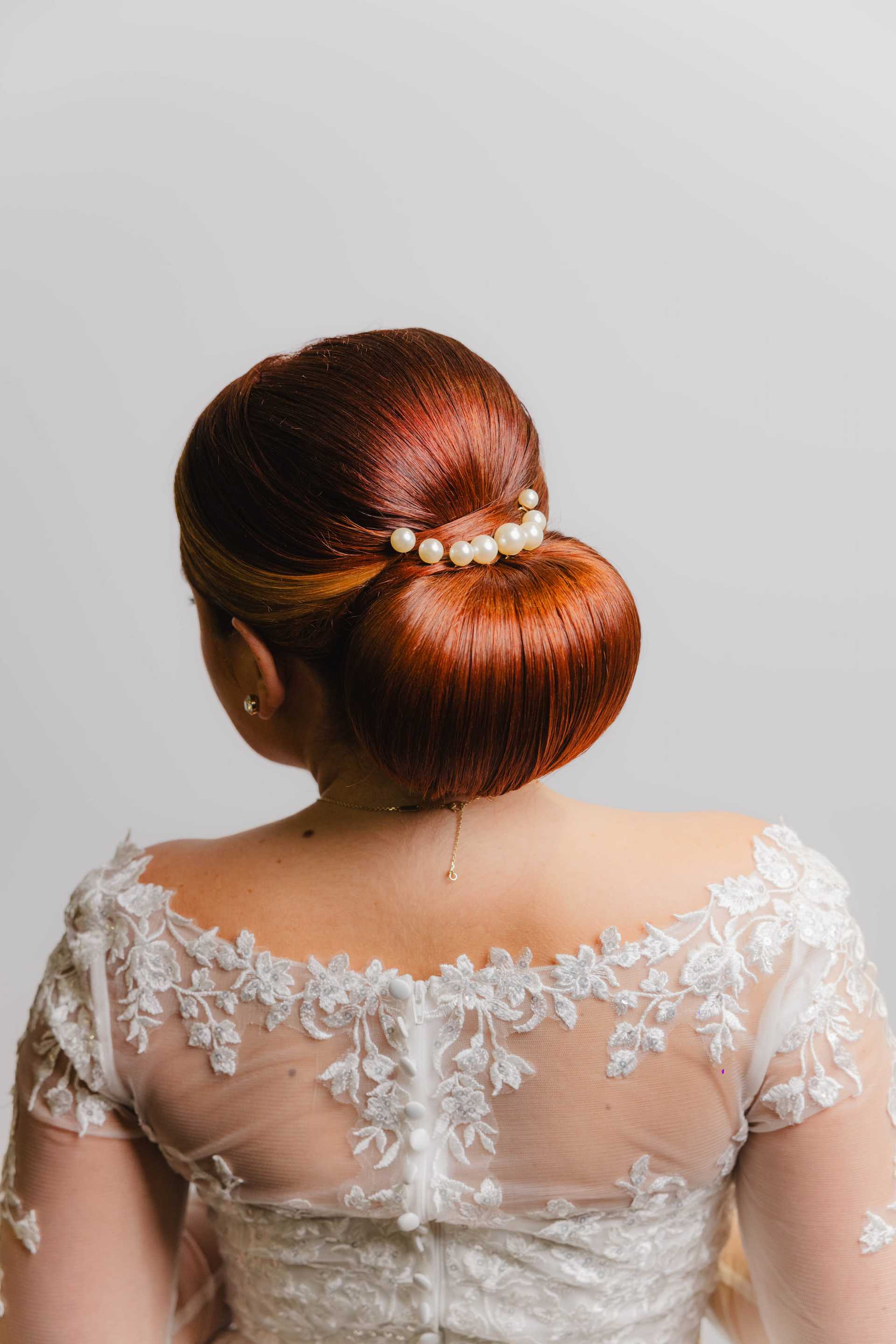 Bride with red hair in an elegant updo adorned with pearls, wearing a lace wedding dress.