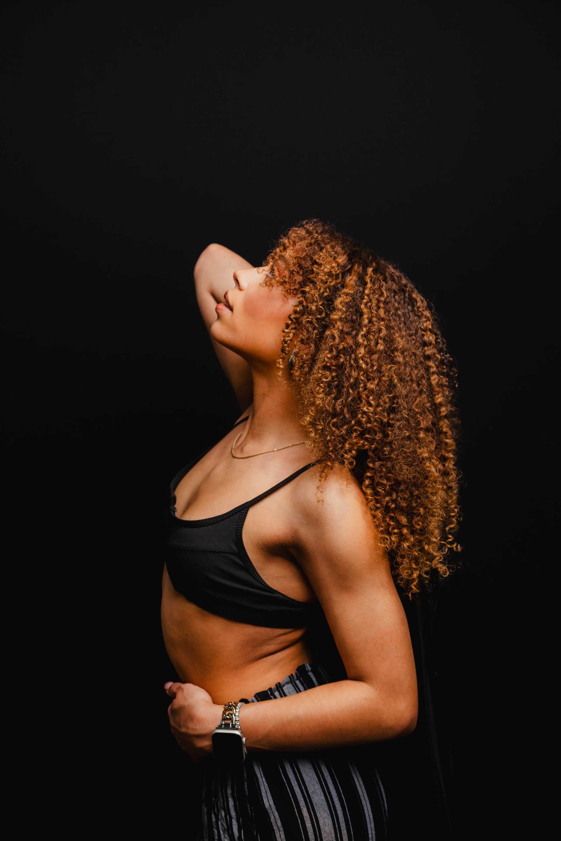 Woman with curly hair poses against a black background, wearing a striped outfit.