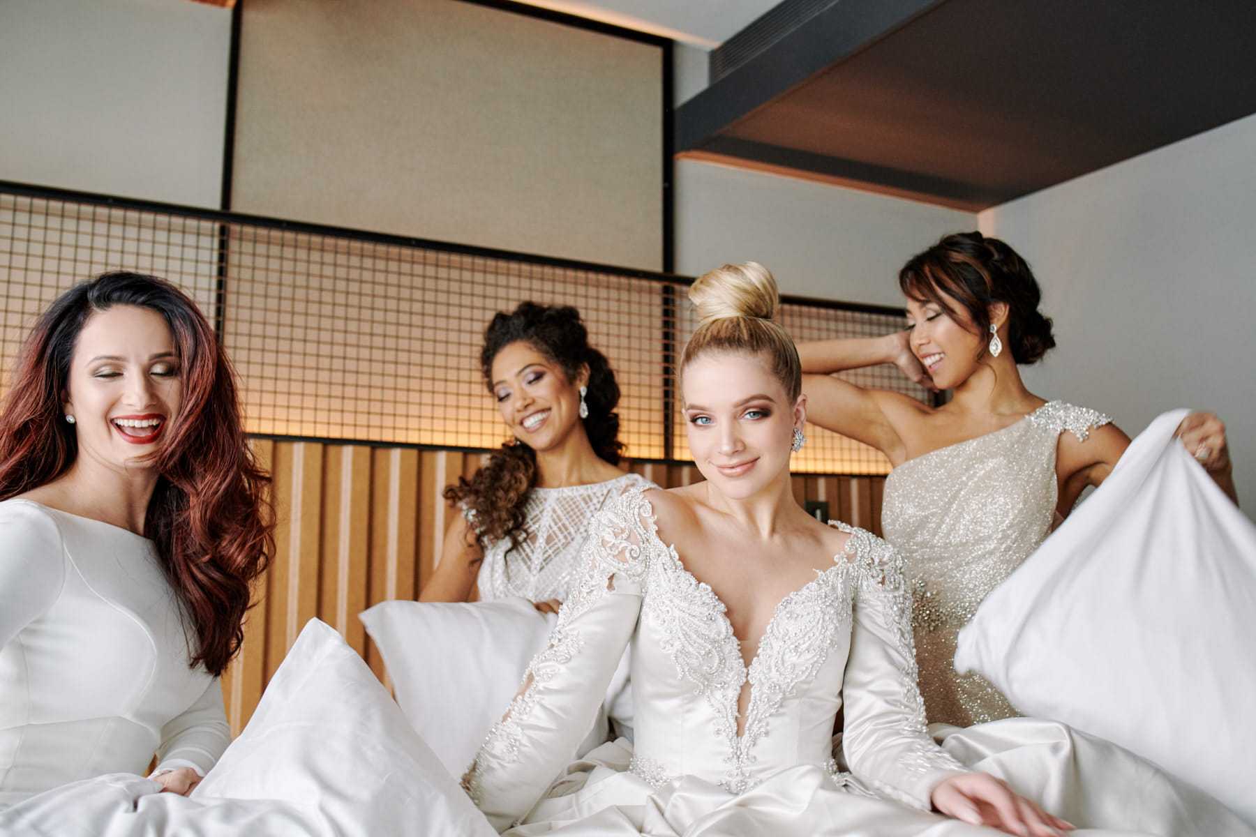 Bridesmaids and bride in elegant dresses relaxing on a bed, smiling and enjoying the moment.