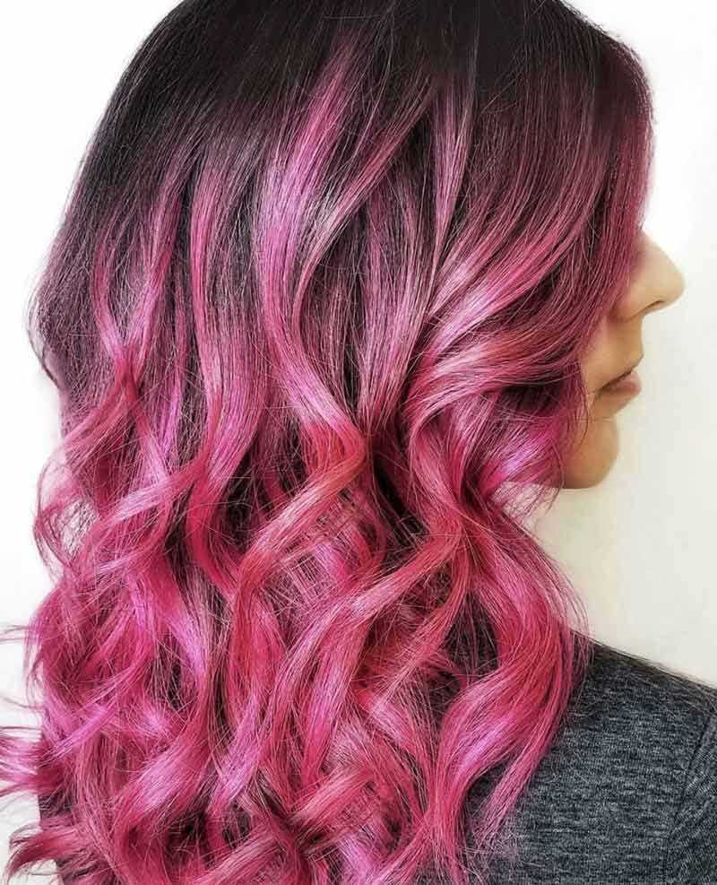 Woman with wavy, pink ombre hair from dark roots.